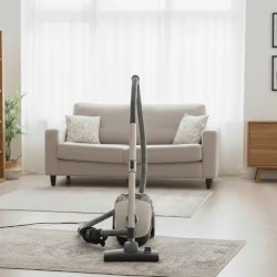 Ein Staubsauger steht vor einem Sofa. Symbolbild.